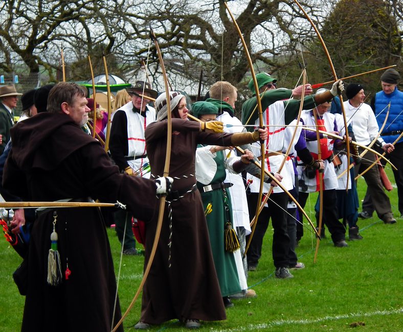 A line of archers in medieval costume shooting longbows