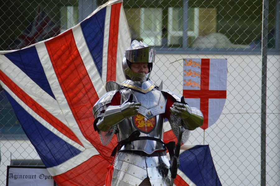 A person wearing a suit of armour in front of historic flags