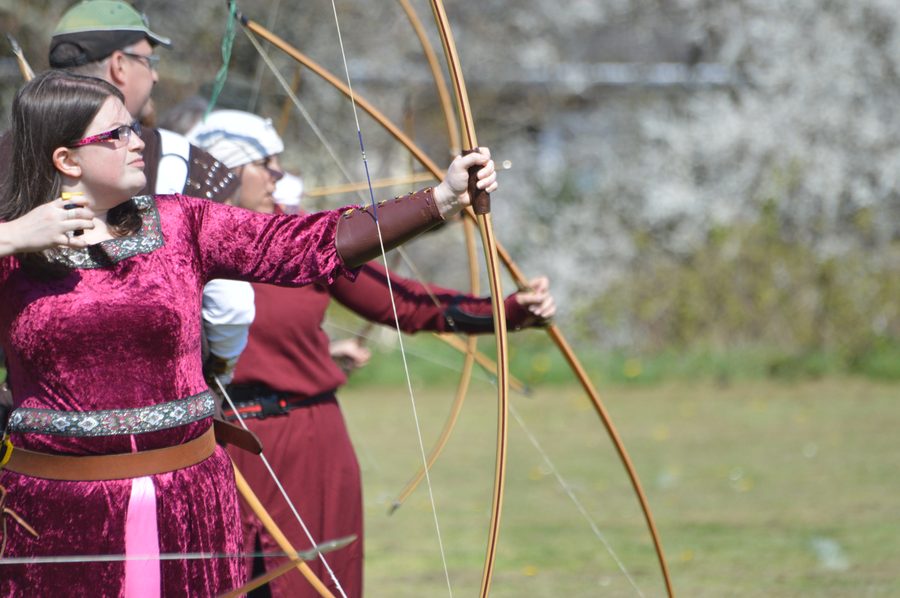 A traditional archer in costume aiming a longbow