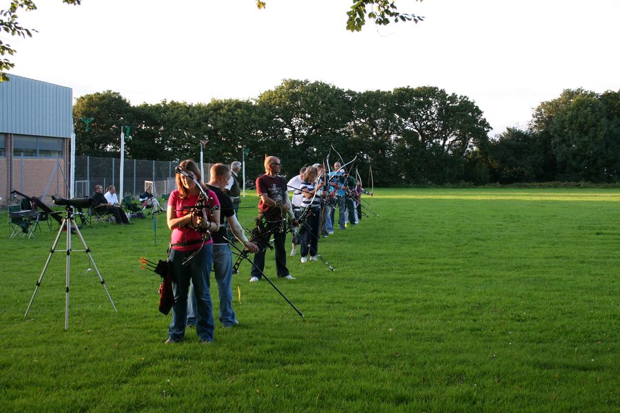 A line of archers with modern bows on a sunny outdoor range